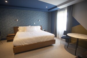 Una habitación de hotel moderna con una cama grande, mesitas de noche, una mesa redonda y una silla.