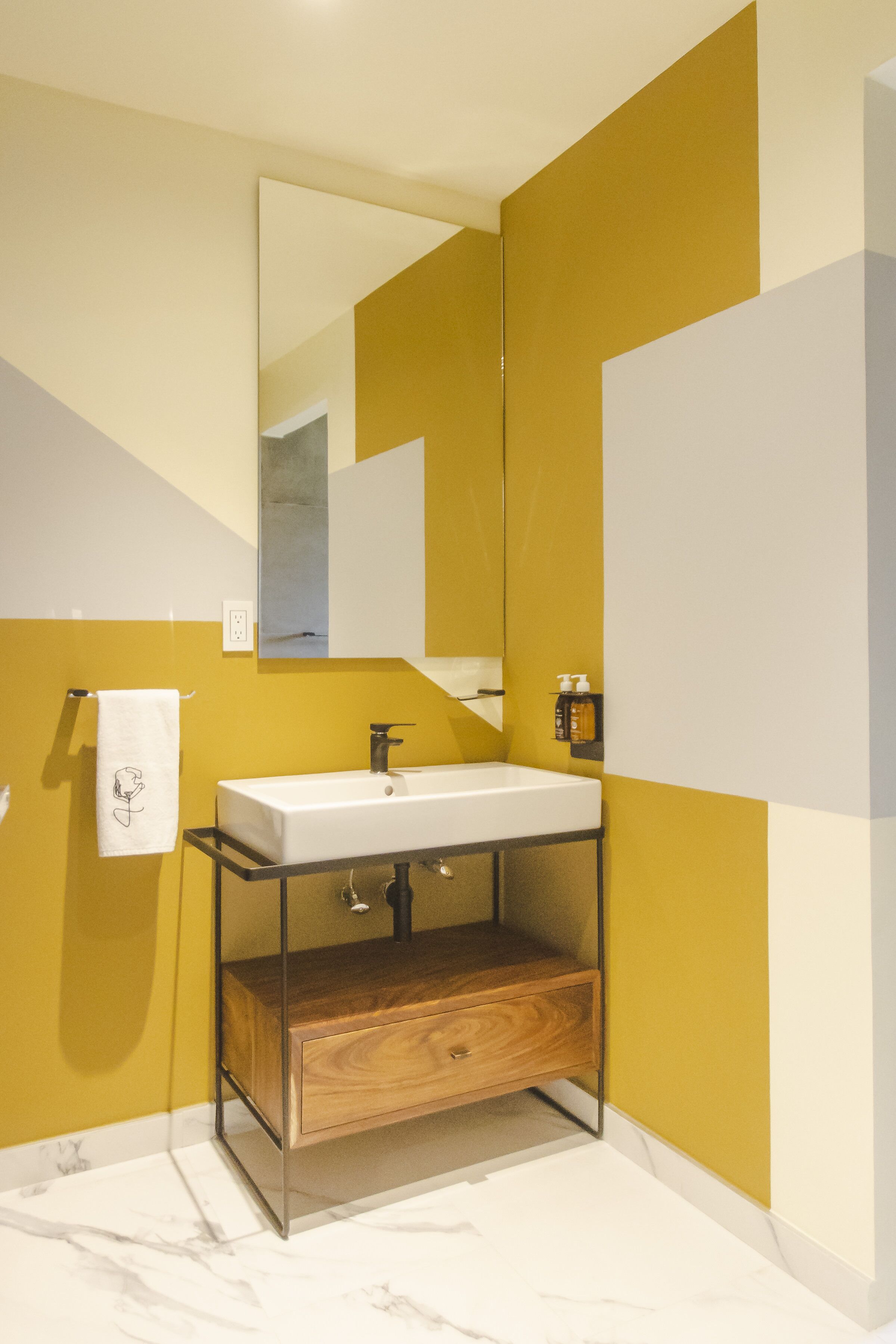 A modern bathroom with a white sink, wooden cabinet, and a large mirror.