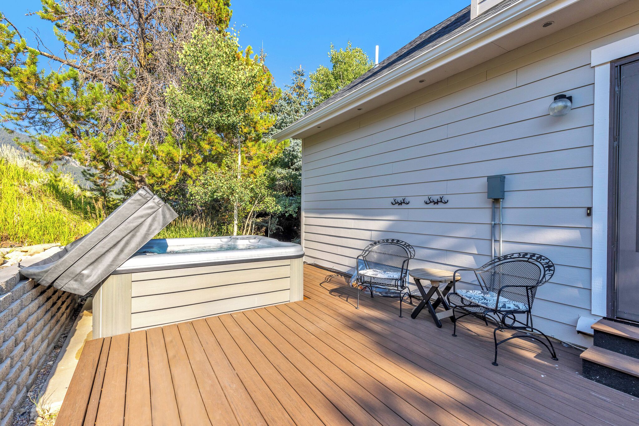 Une terrasse en bois avec un jacuzzi, deux chaises en métal et un espace abrité.