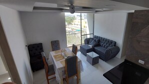 Ein modernes Wohnzimmer mit grauem Sofa, einem Esstisch mit Stühlen und einem Balkon mit Blick auf Gebäude.