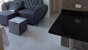 Ein modernes Wohnzimmer mit einem grauen Ecksofa, einem Glastisch und einem schwarzen Esstisch.