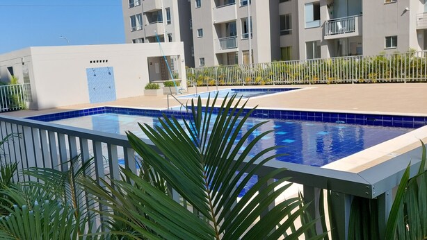Ein rechteckiger Swimmingpool mit einer gefliesten Kante, umgeben von einem weißen Zaun und üppigem Grün.