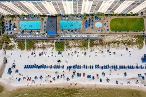 Vista aerea di un hotel con diverse piscine, una spiaggia attrezzata con ombrelloni e un grattacielo sullo sfondo.