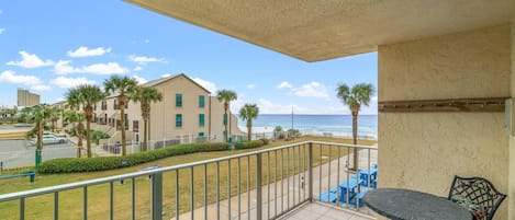 A balcony with a view of the beach, a table and chairs, and a railing.