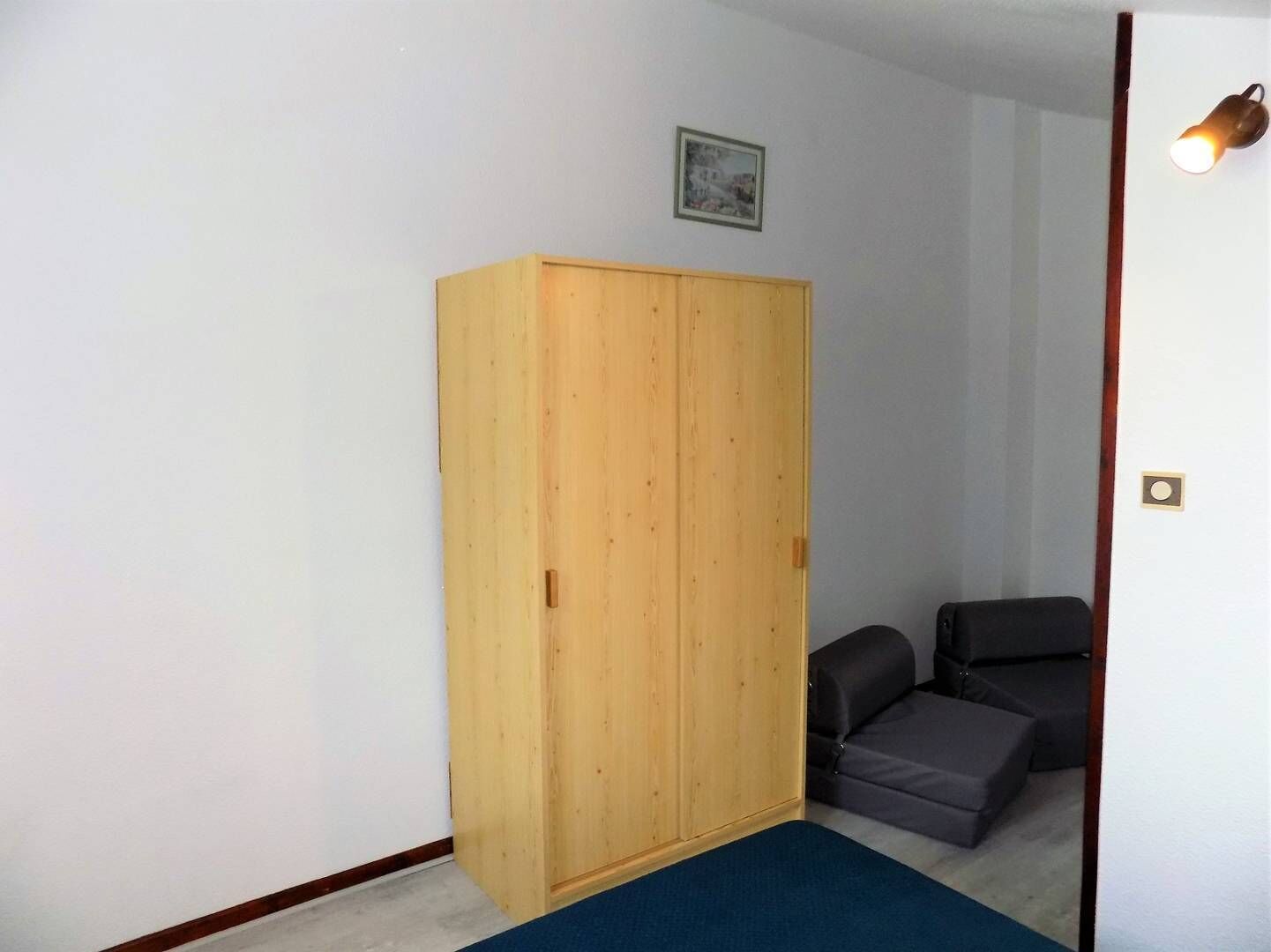 Una habitación con un armario de madera, un sofá gris y una alfombra pequeña.