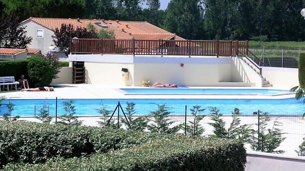 Une piscine avec une terrasse en bois et une maison en arrière-plan.