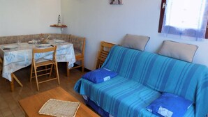 Un salon chaleureux avec un canapé à rayures bleues, une table à manger dressée pour deux personnes et un petit coin cuisine.