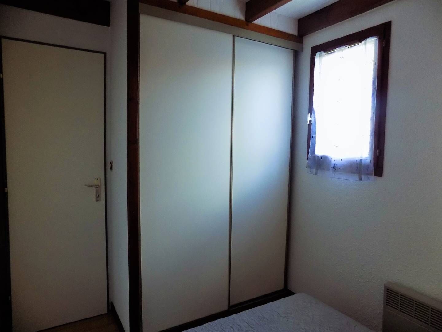 A room with a sliding door, a small window with a curtain, and a radiator.