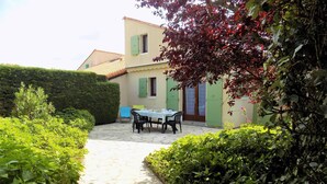 Un chemin de pierres mène à une table dressée pour deux personnes, dans un coin jardin, avec un bâtiment visible en arrière-plan.