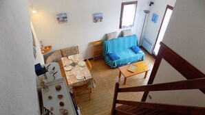 Un coin repas avec une table dressée pour deux personnes, un canapé et un escalier menant à l’étage supérieur.