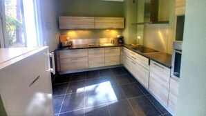 Una cocina moderna con armarios de madera clara, un refrigerador de acero inoxidable y piso de baldosas negras.