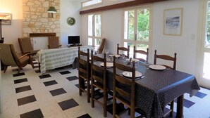 Comedor con suelo a cuadros, sillas de madera, una mesa dispuesta para cuatro, pared de piedra y una lámpara colgante.