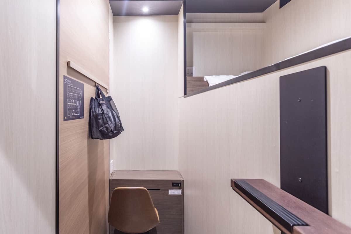 A narrow hallway with a wooden wall, a black door, a chair, and a small desk with a computer.