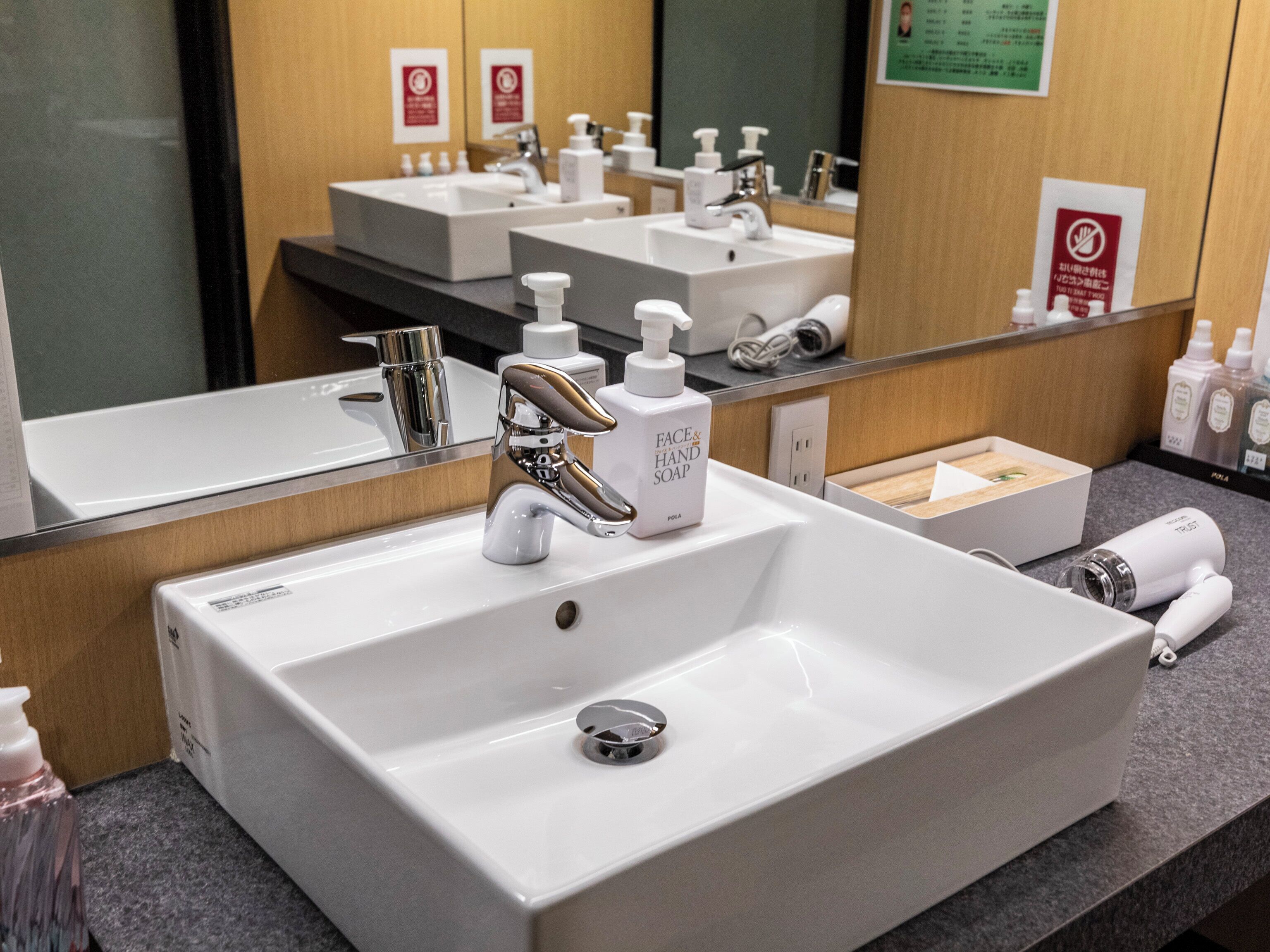Een hotelbadkamer met een witte wastafel, een chromen kraan en diverse toiletartikelen.