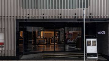 A hotel entrance with a modern design, featuring a glass facade and a sign that reads "TRUST HOTEL".