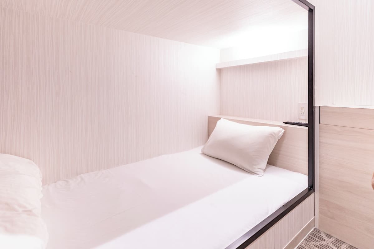 Habitación minimalista con una cama individual, cabecera de madera y pared de color claro.