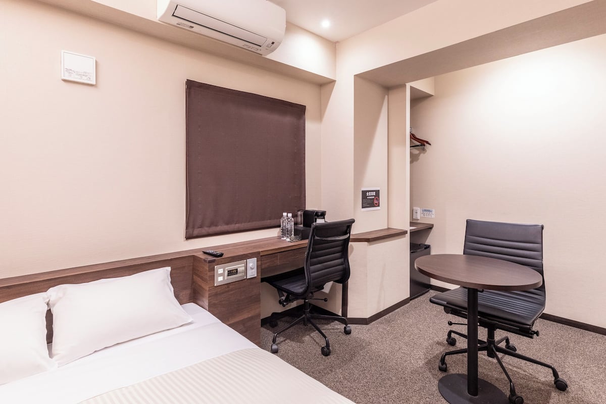 Habitación de hotel con cama, escritorio, dos sillas, unidad de aire acondicionado y una mesita.
