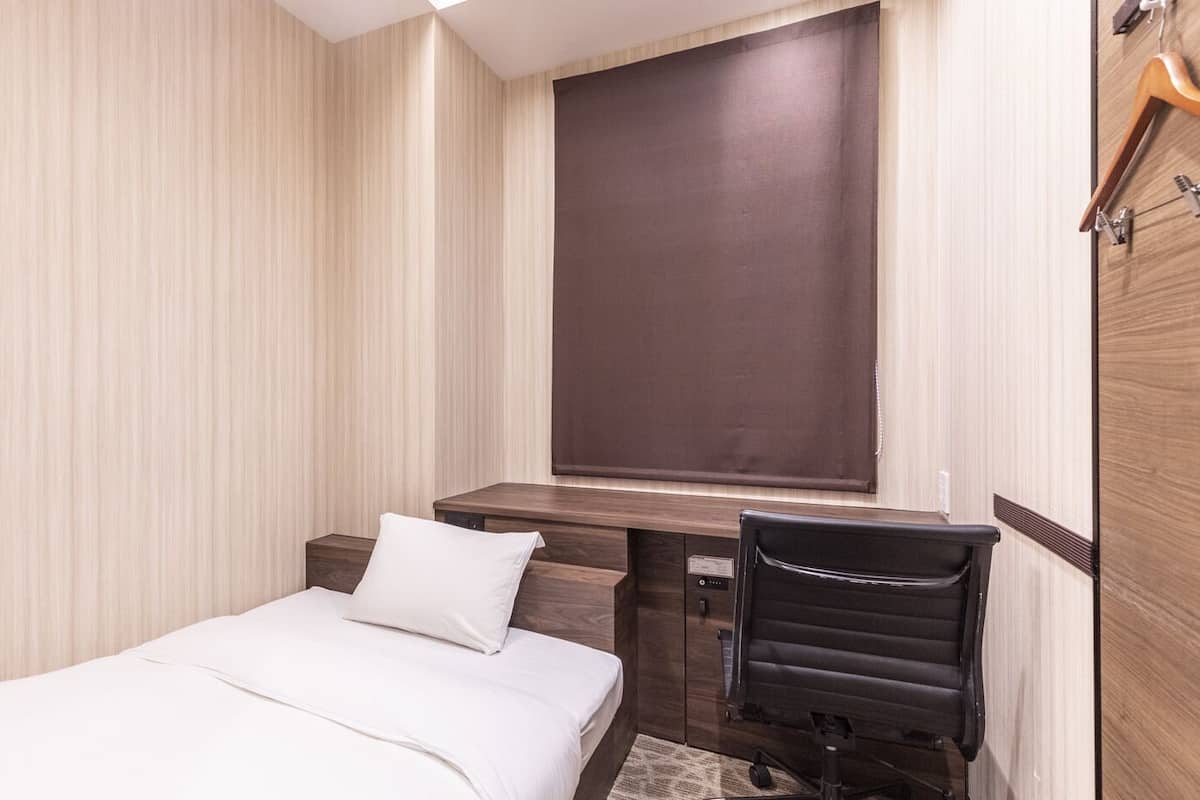 A hotel room with a bed, a desk, a chair, and a window.
