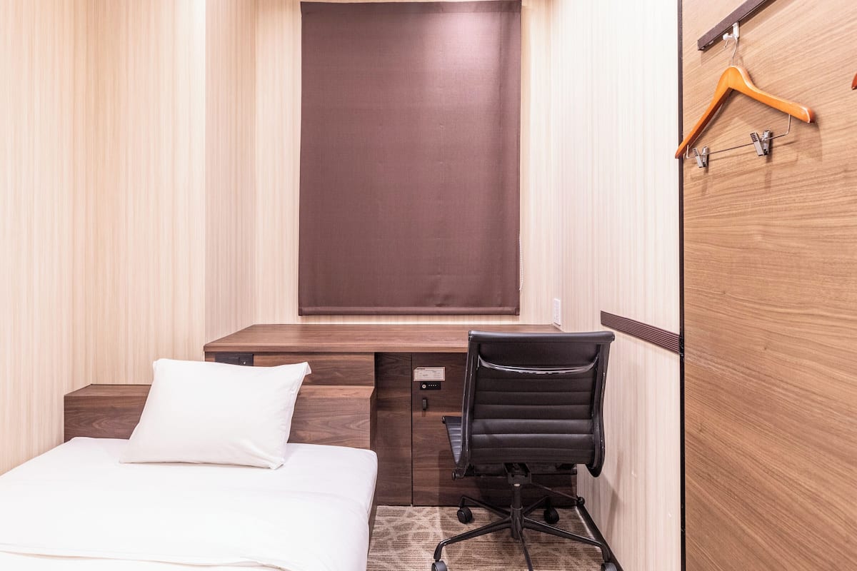 Una habitación de hotel compacta con cama, escritorio, silla y armario.