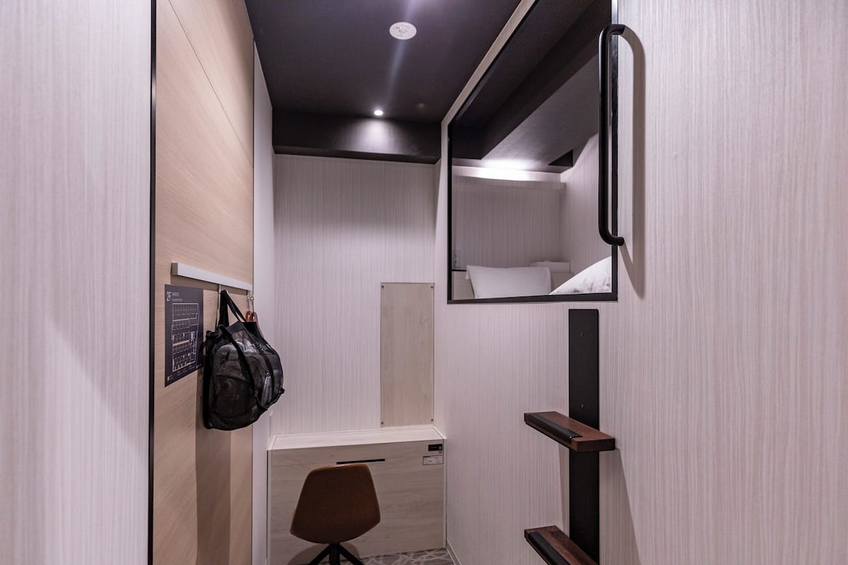 Habitación de hotel compacta con armario espejado, un escritorio pequeño y una silla.