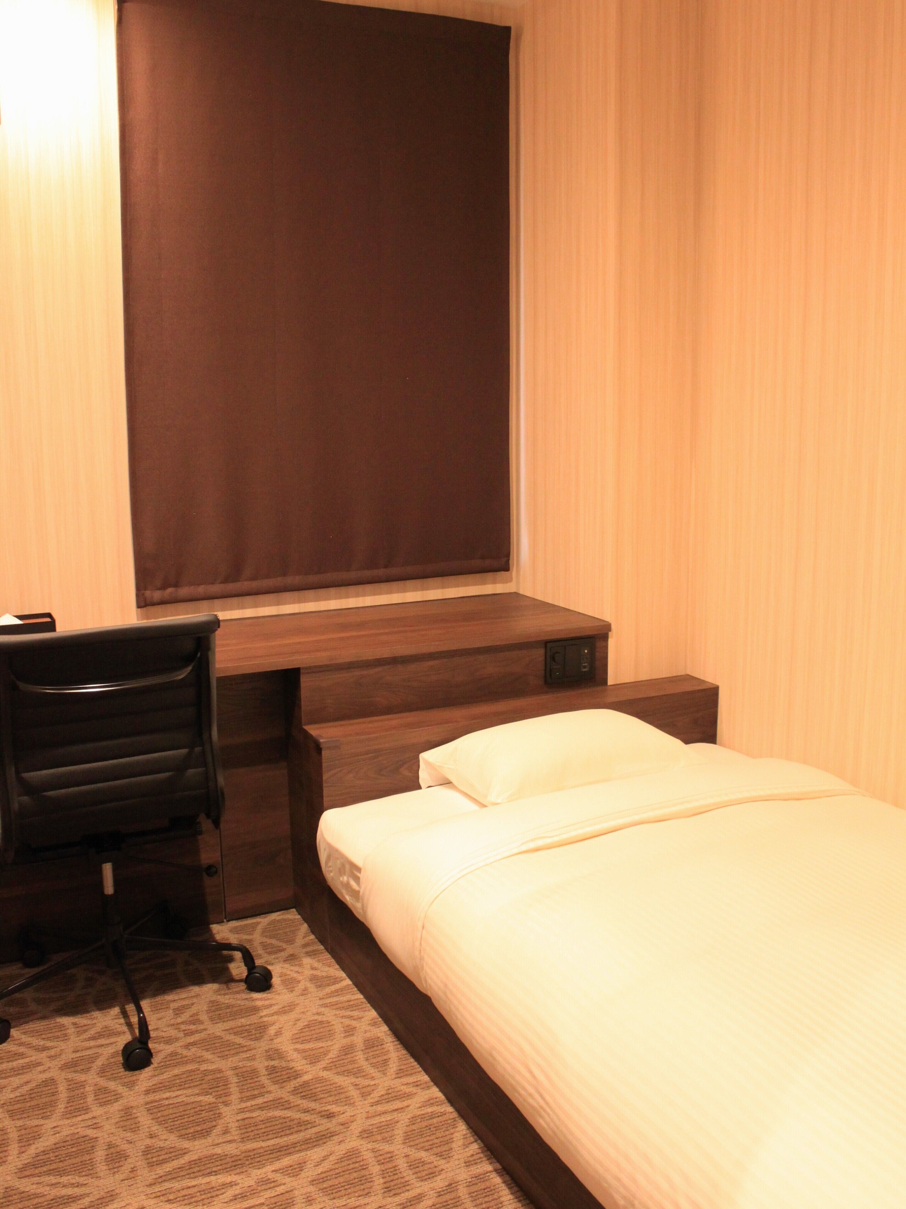 A hotel room with a bed, a desk, a chair, and a window with curtains.