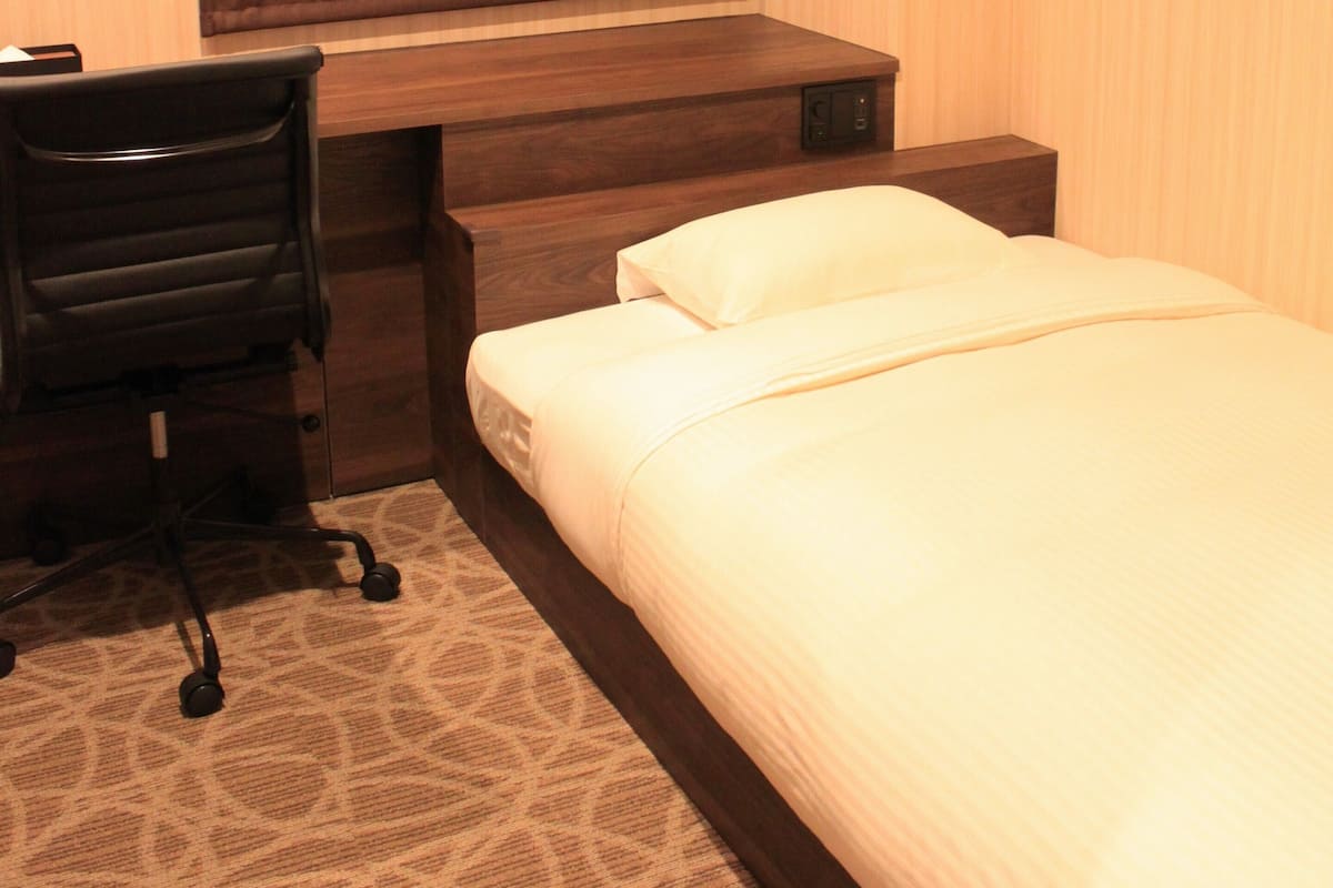 A hotel room with a bed, a desk, a chair, and a window with curtains.