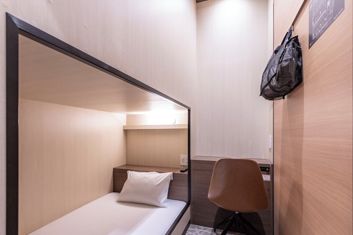 Habitación de hotel pequeña con literas, un escritorio, una silla y un bolso colgado en la pared.