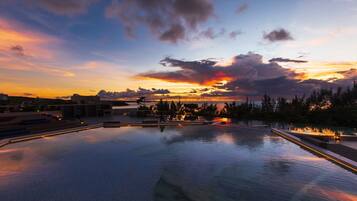 A swimming pool with a sunset view, surrounded by trees and buildings.