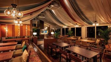A spacious restaurant with wooden tables and chairs, a bar area, and large windows.