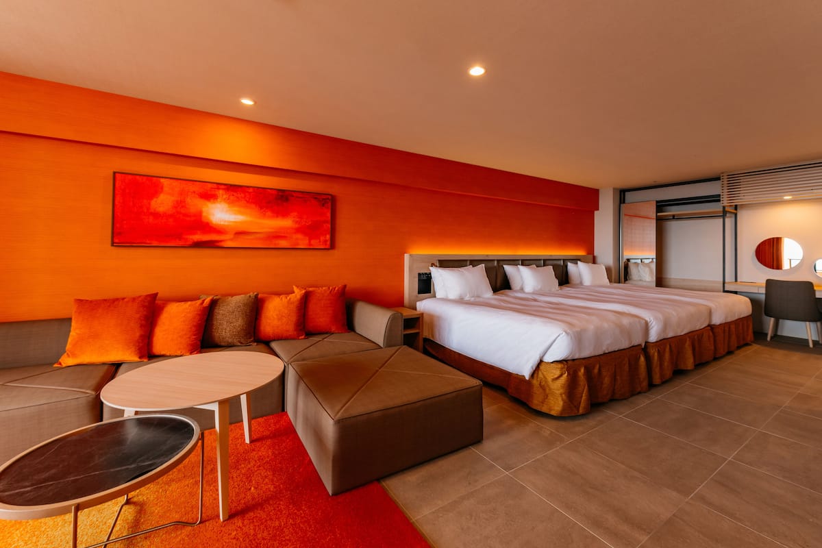 Quarto de hotel moderno com uma cama grande, um sofá, uma mesinha e um tapete vermelho.