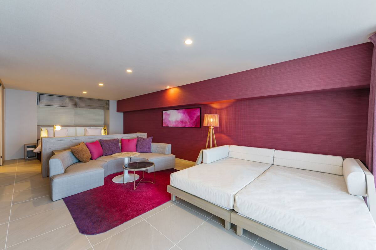 Quarto de hotel moderno com sofá, cama, mesinha e tapete vermelho.