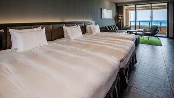 Habitación de hotel con dos camas grandes, un sofá, una mesita y vista al océano.