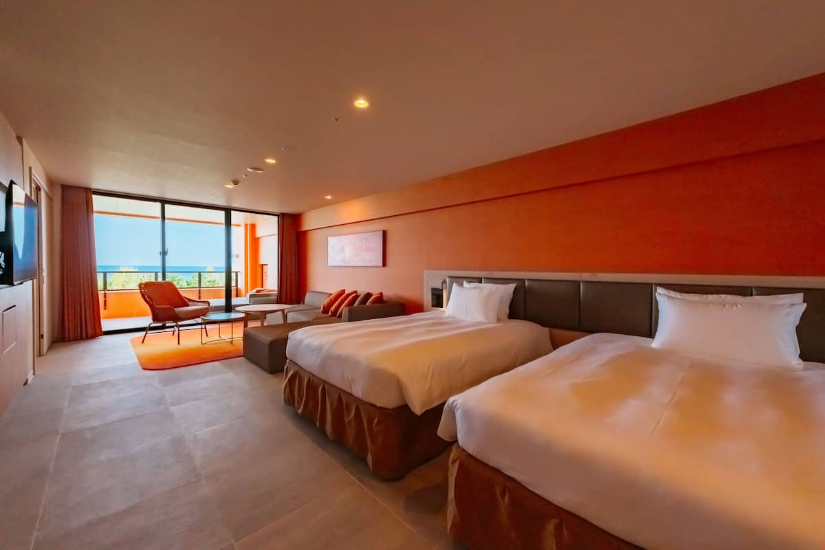 Quarto de hotel com duas camas, um sofá, uma mesa de jantar e vista para o mar.