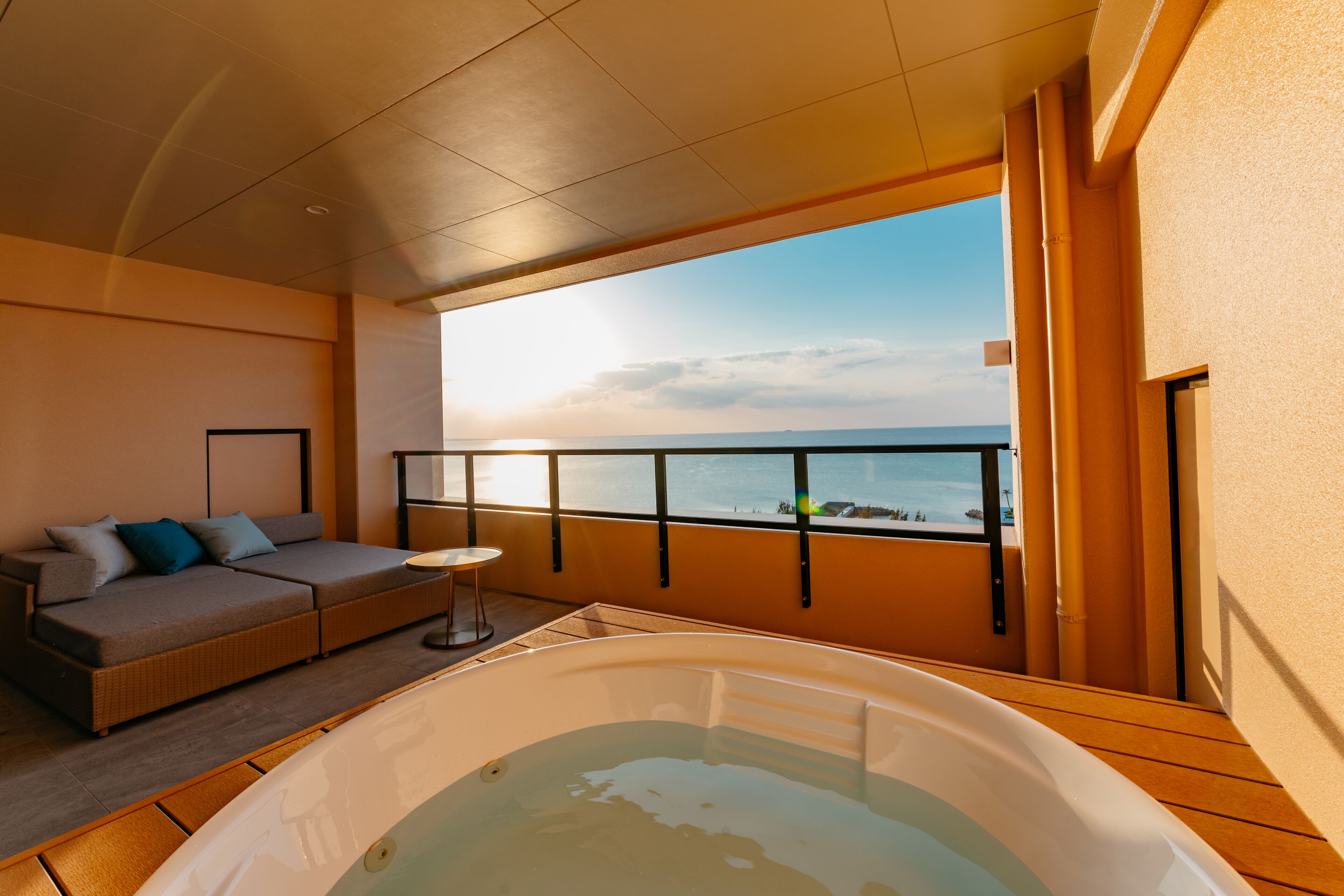 A balcony with a hot tub, a sofa, and a view of the sea.