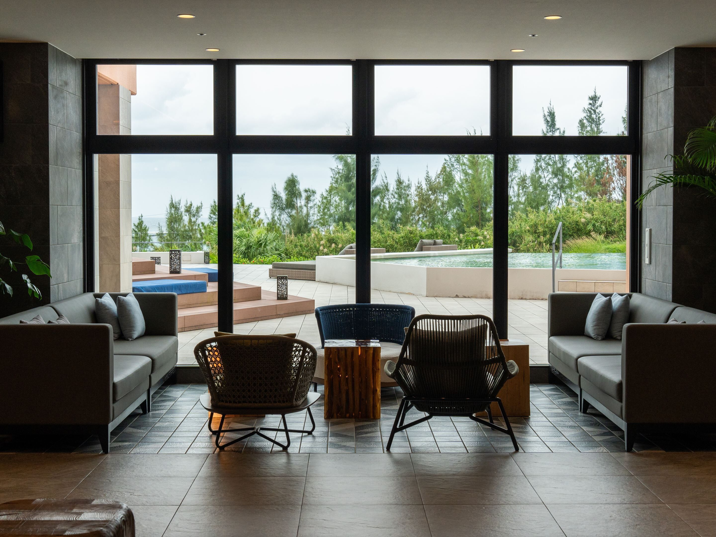 Amplia sala de estar con grandes ventanales, piscina y mobiliario exterior.