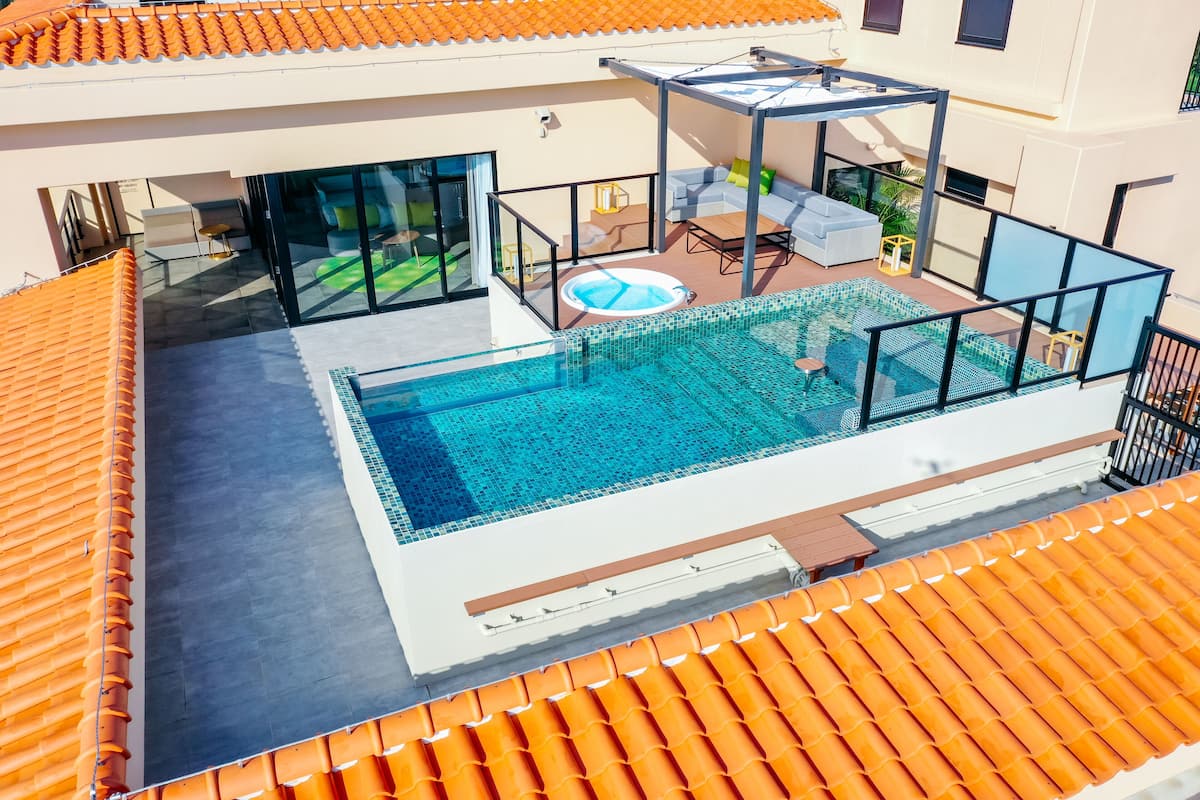 Uma piscina no terraço com estrutura de vidro, um solário com assentos e uma área coberta com mesa e cadeiras.