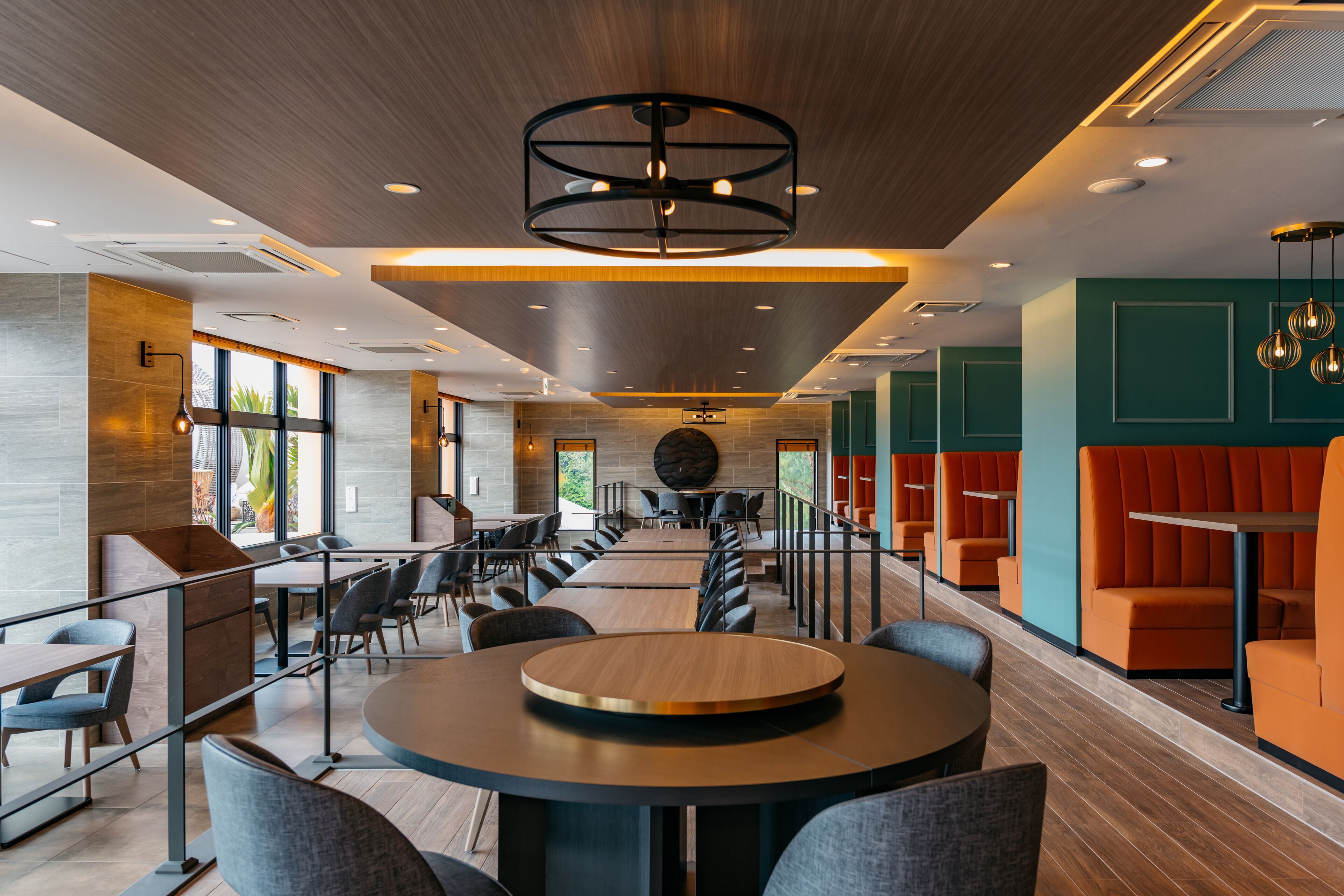 A modern indoor space with a long dining table, multiple seating areas, and a central circular light fixture.