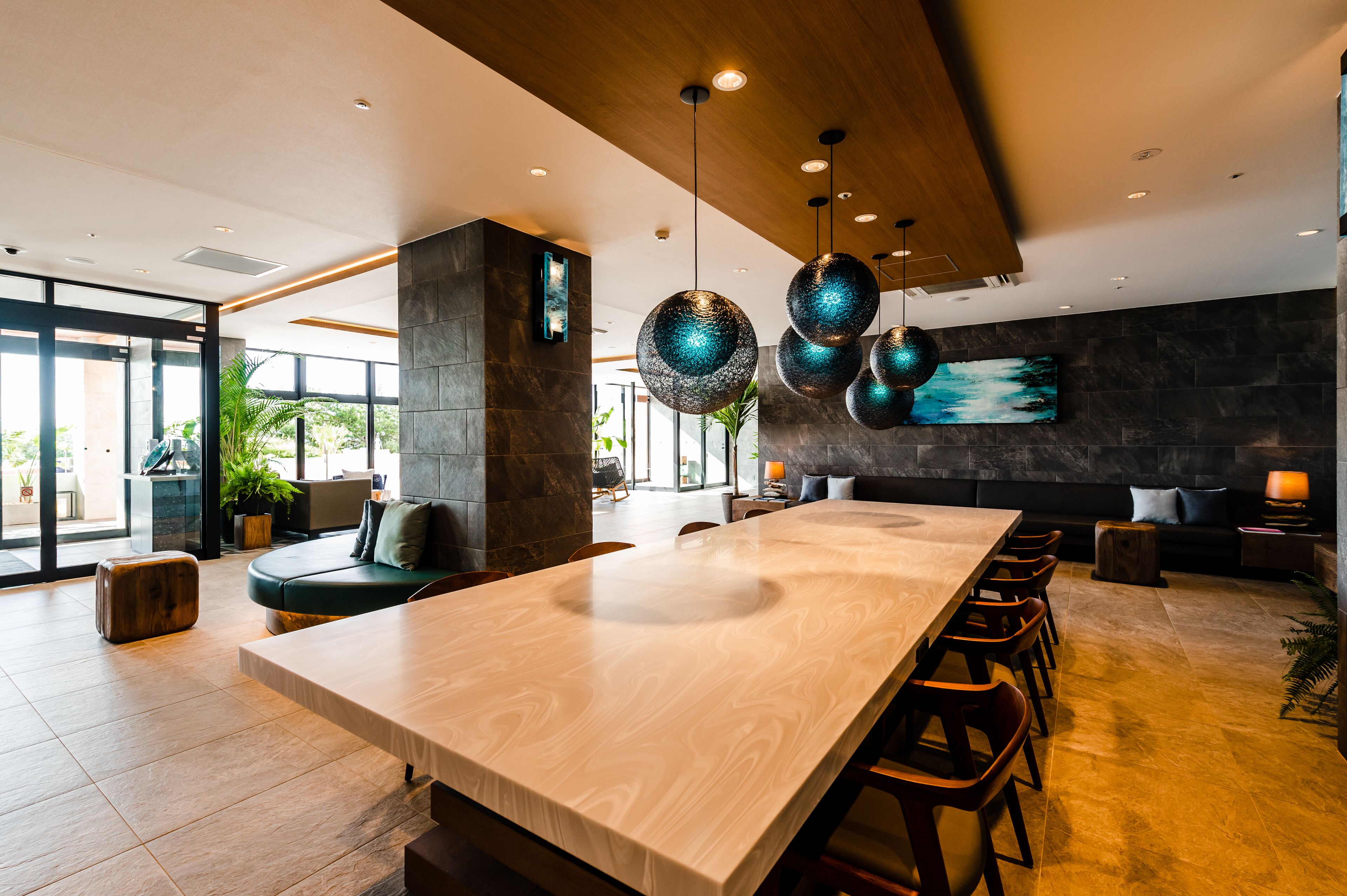A modern interior with a long wooden table, dark stone walls, and hanging spherical light fixtures.