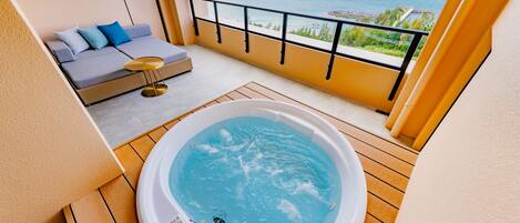 A balcony with a hot tub, a sofa with cushions, and a view of the sea.