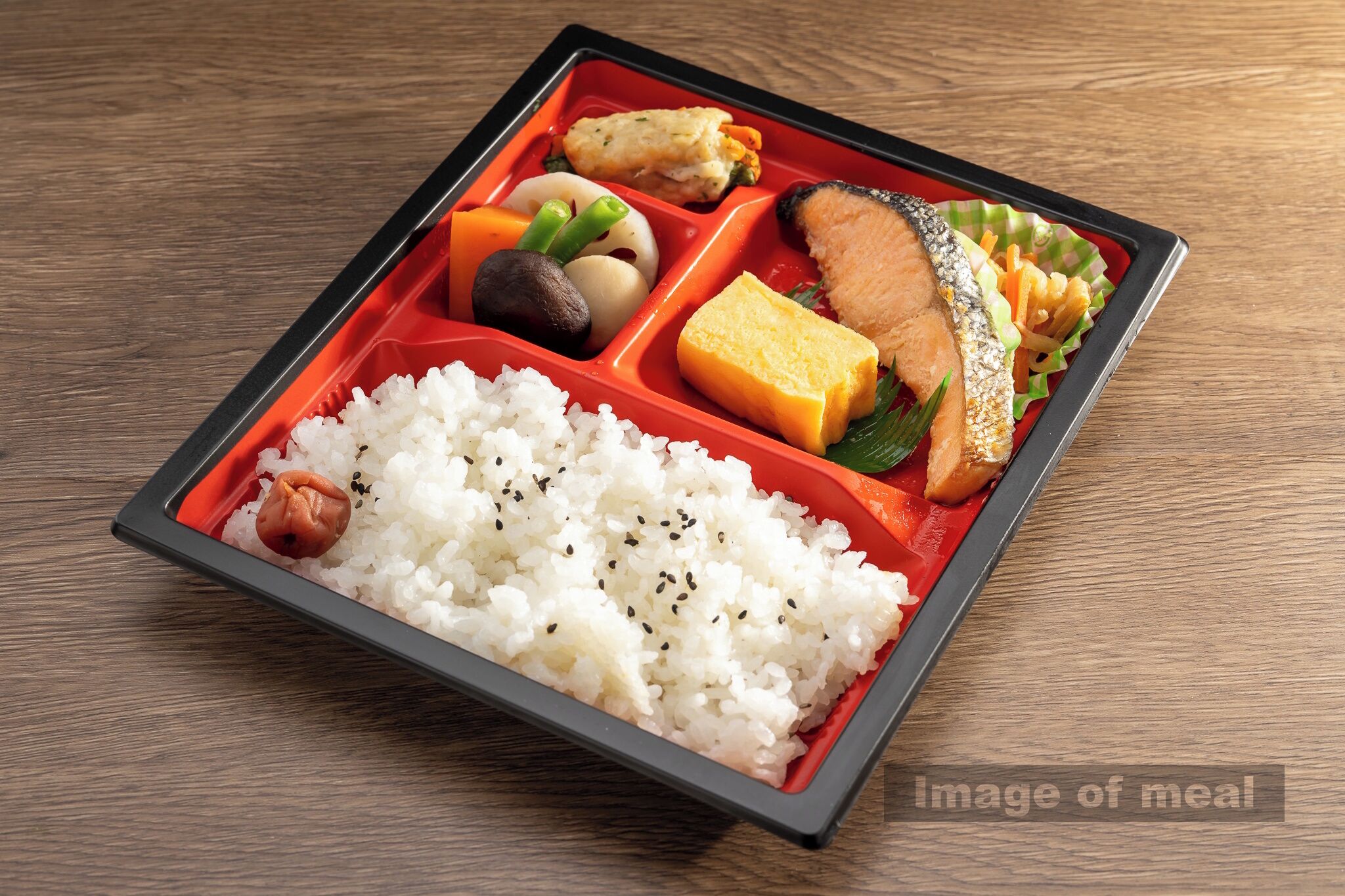 A bento box with rice, fish, tofu, and vegetables on a wooden table.