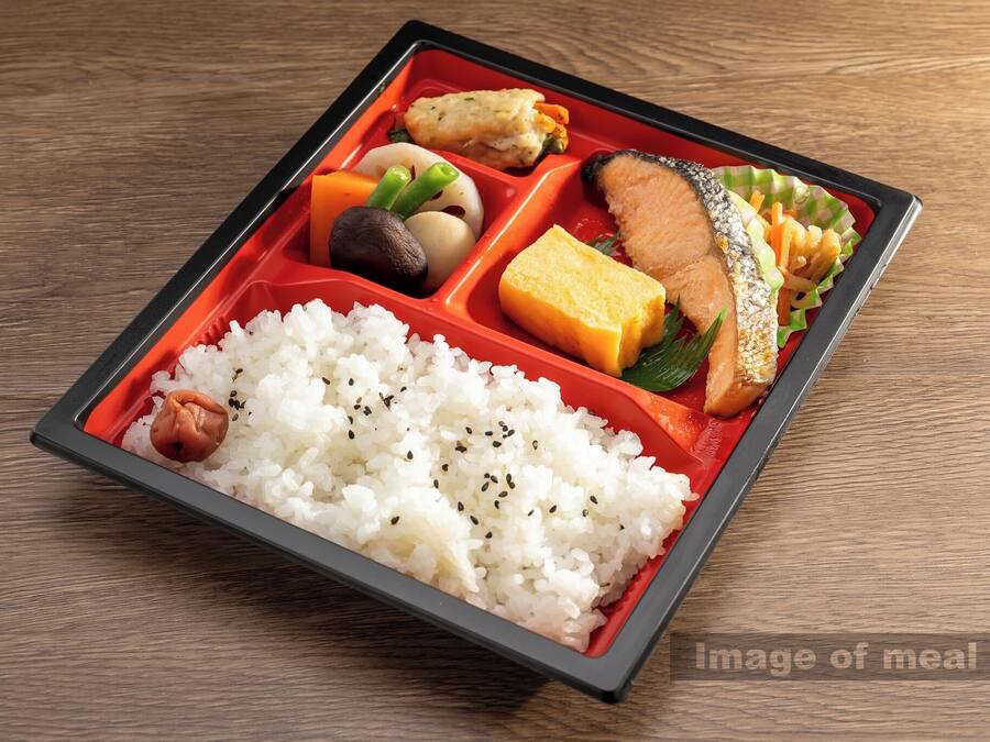 A bento box with rice, fish, tofu, and vegetables on a wooden table.