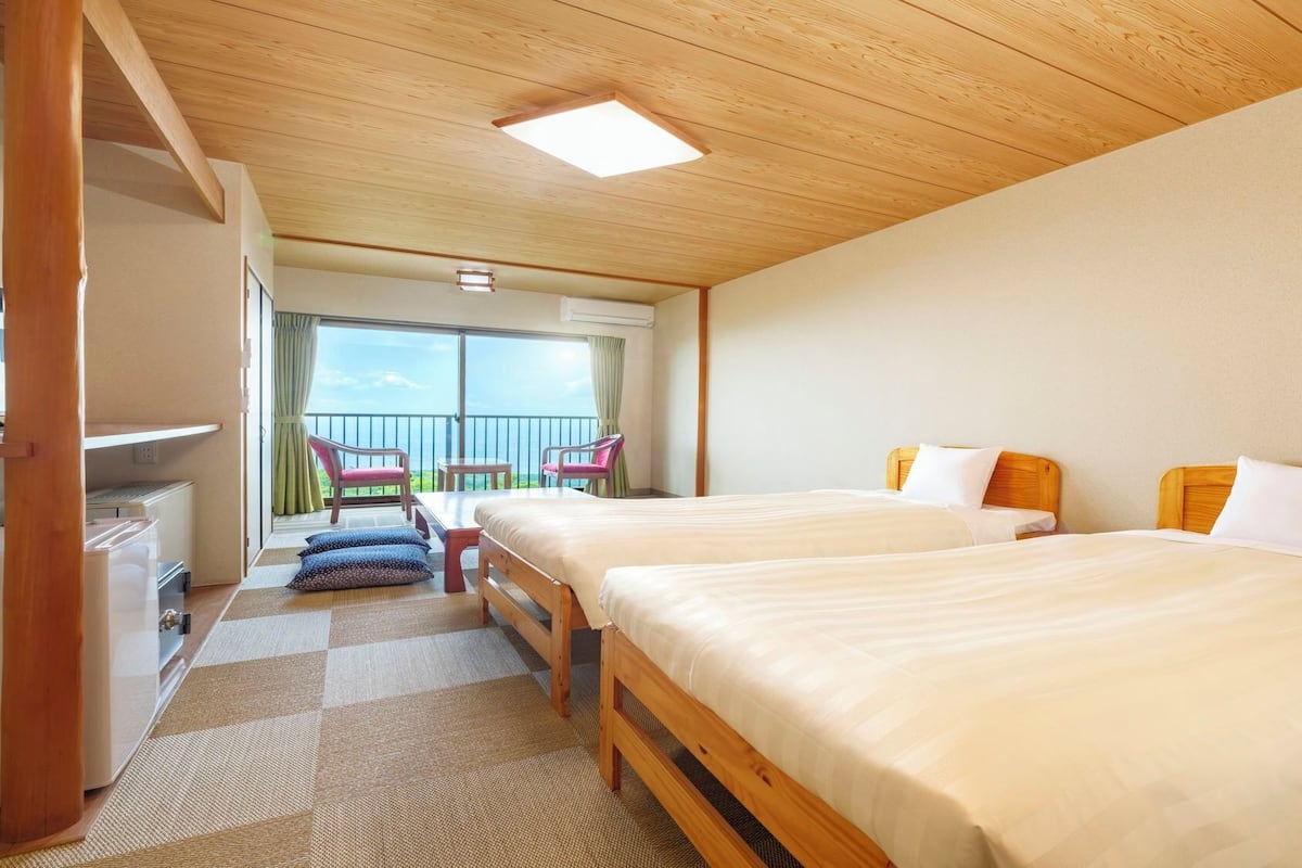 Ein Hotelzimmer mit zwei Betten, einem Balkon mit Stühlen und Meerblick.