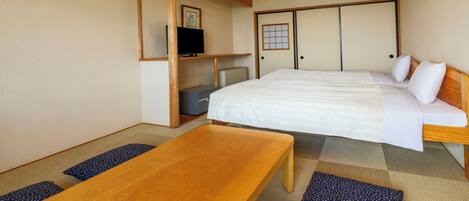 A traditional Japanese-style room with tatami flooring, a wooden bed with white bedding, a television on a shelf, and a sliding door.