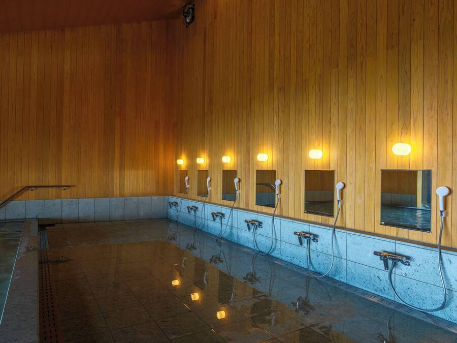 A public shower area with multiple showerheads and mirrors on wooden walls.