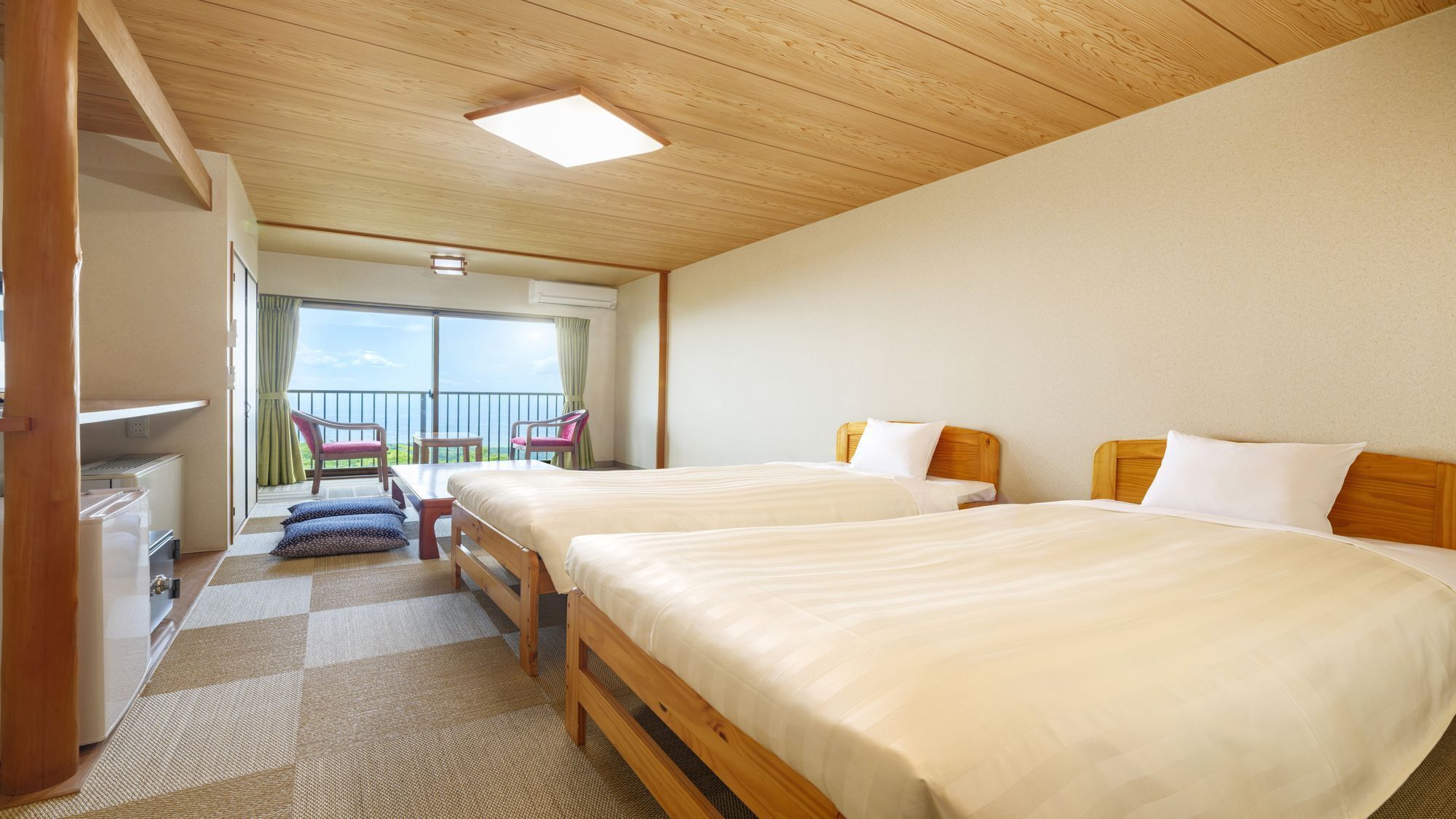 A hotel room with two beds, a balcony with chairs, and a view of the sea.