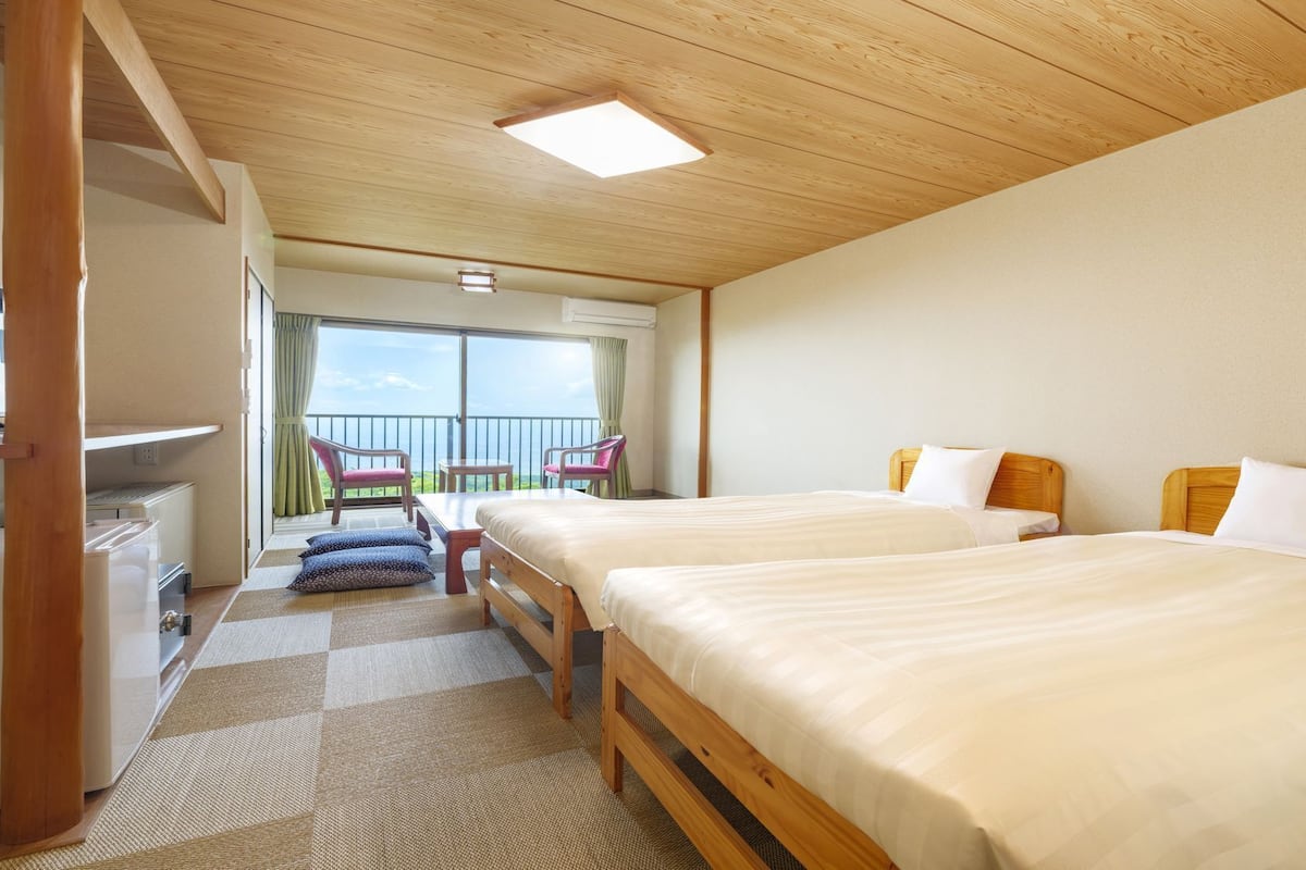 Ein Hotelzimmer mit zwei Betten, einem Balkon mit Stühlen und Blick auf das Meer.