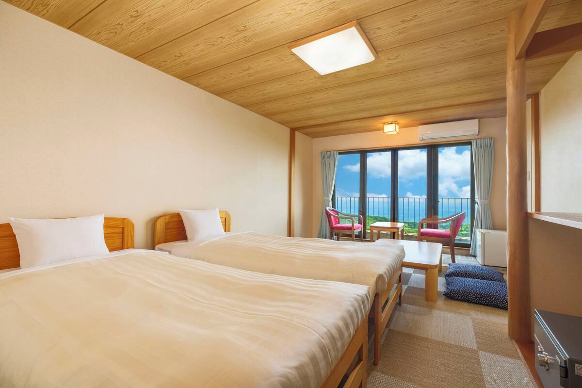Ein Hotelzimmer mit zwei Betten, einem kleinen Tisch, Stühlen und einem Balkon mit Blick.