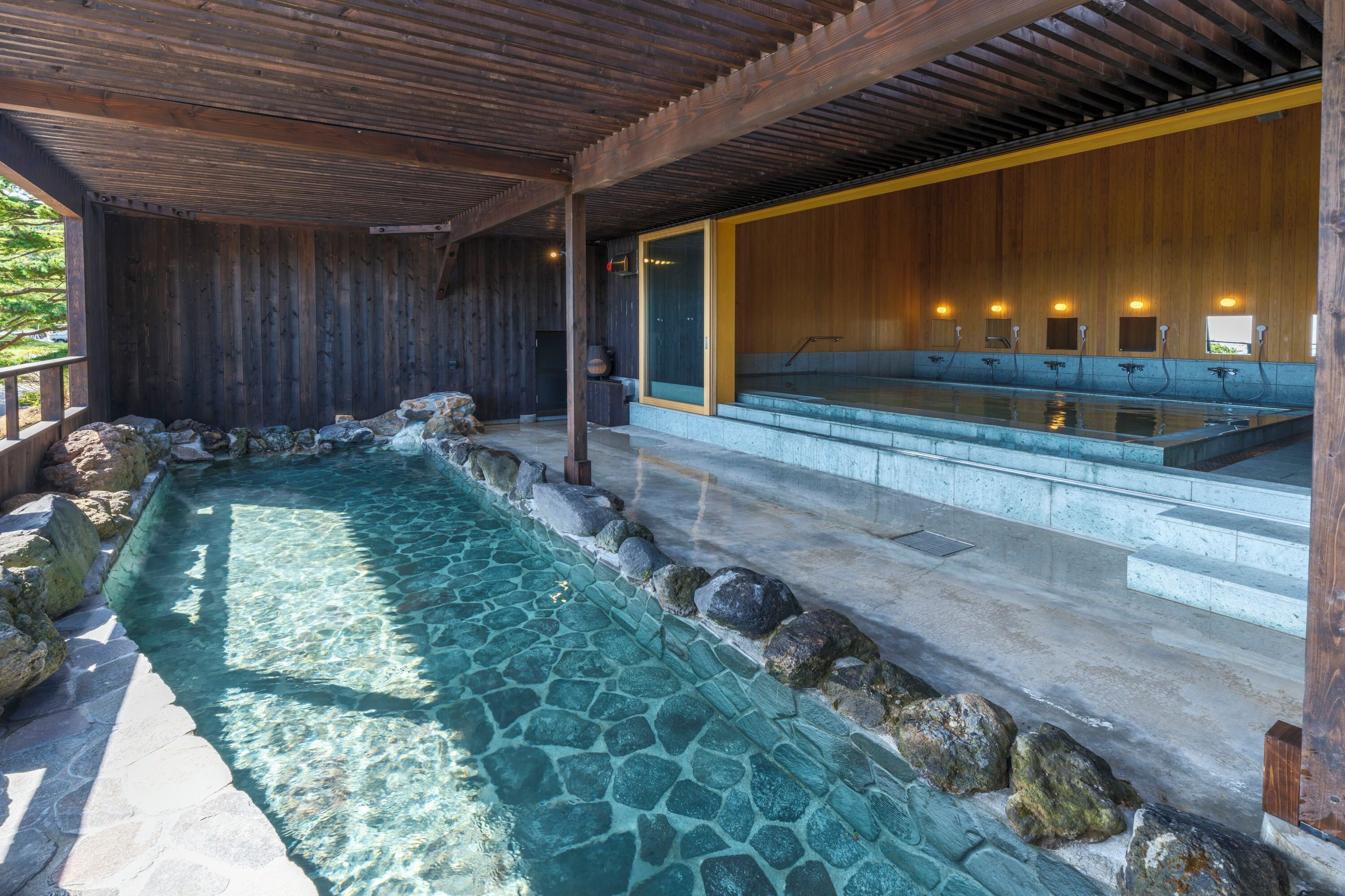 Un espace de détente en bois doté d’une piscine bordée de pierres, de bancs en bois et d’un mur en bois avec une fenêtre.