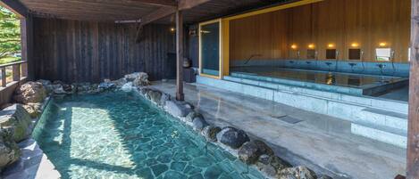 Un espace de détente en bois doté d’une piscine bordée de pierres, de bancs en bois et d’un mur en bois avec une fenêtre.