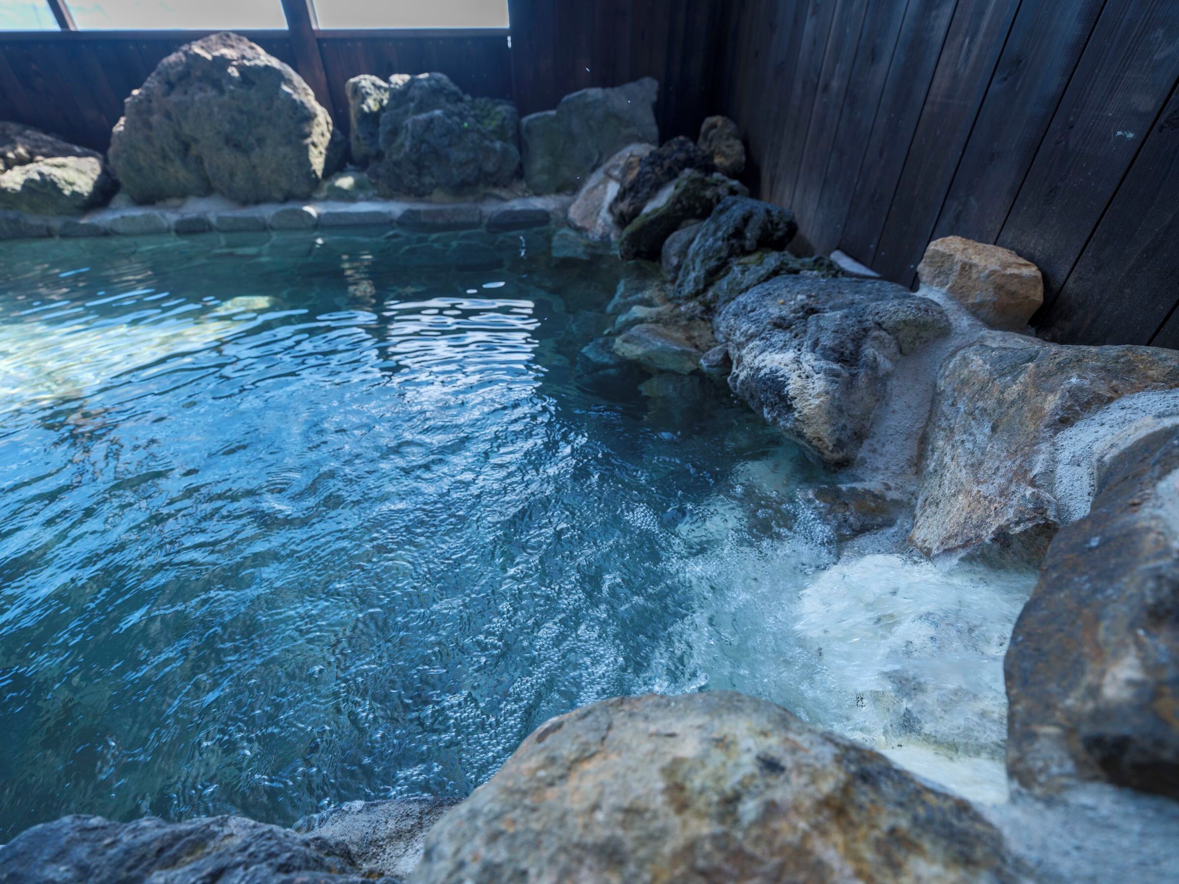 Un manantial termal con agua cristalina, rodeado de rocas grandes y paredes de madera.